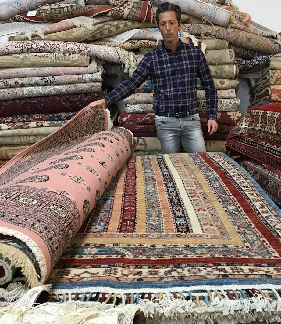 Homme présentant des tapis colorés.